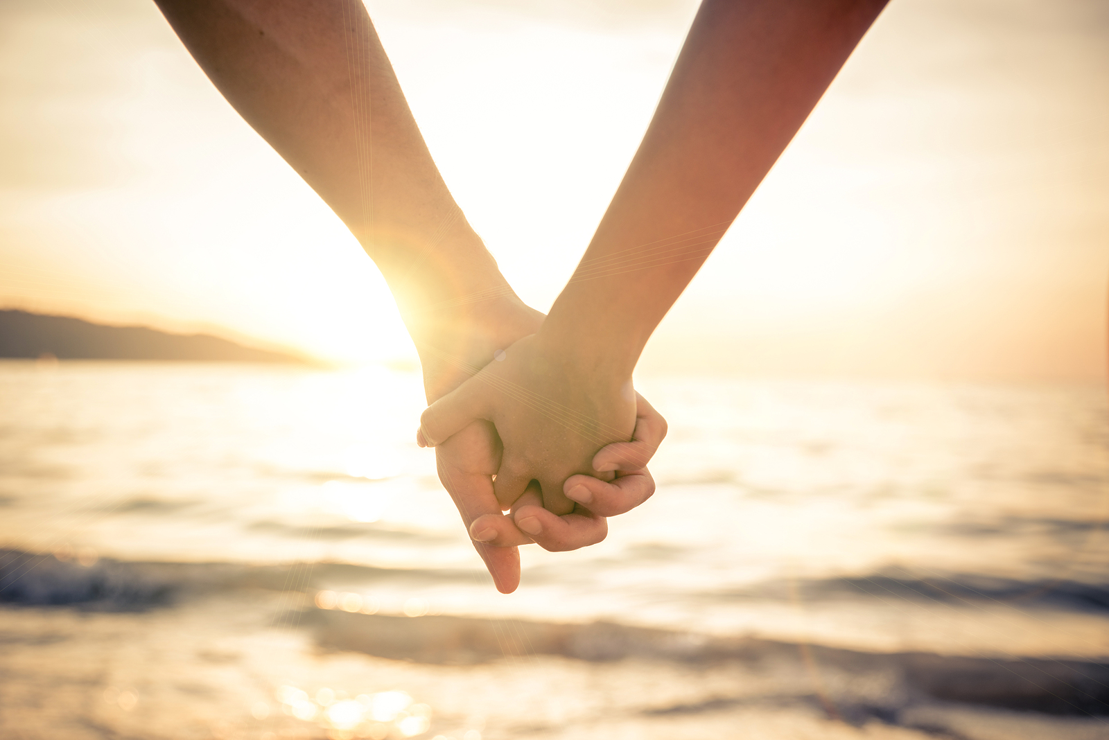 Couple of lovers holding their hands at a beautiful sunset over the ocean -...